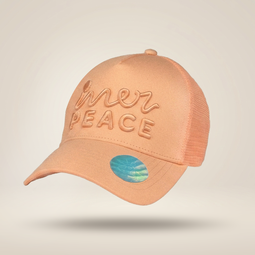 A peach-colored trucker cap with 'mer PEACE' embroidered on the front, set against a light beige background.