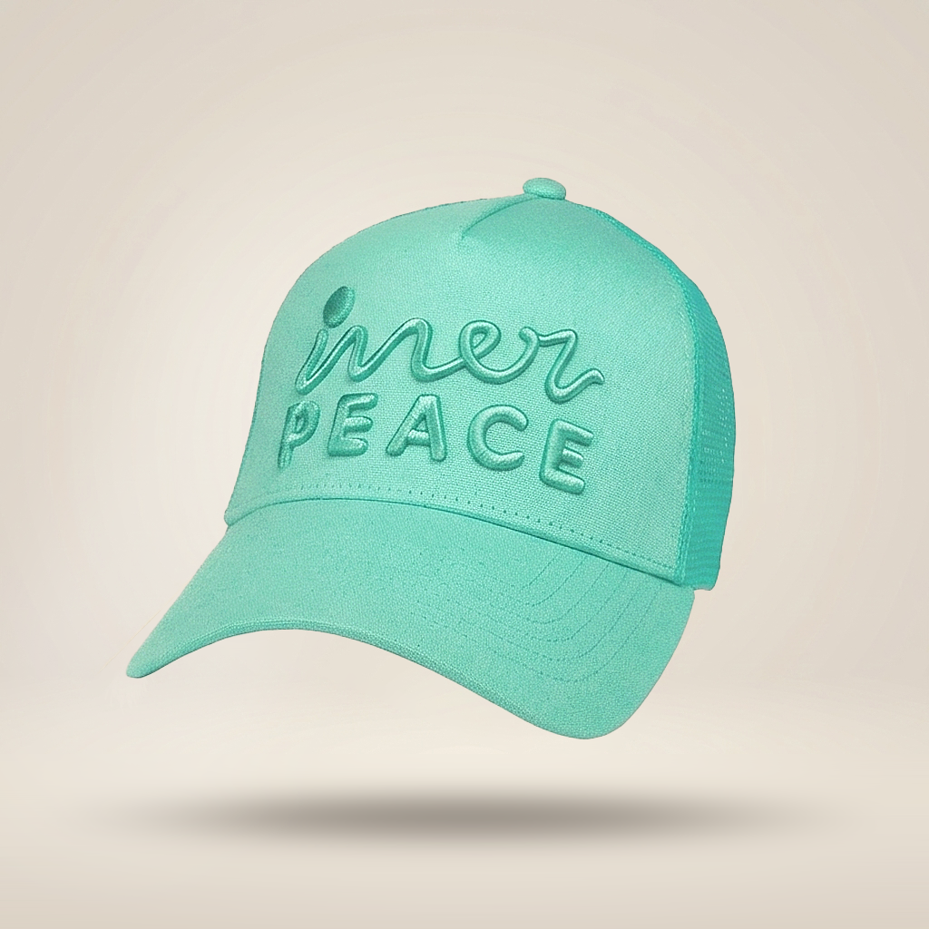 A mint green trucker-style cap with 'inner peace' embroidered on the front, shown floating against a warm beige background.