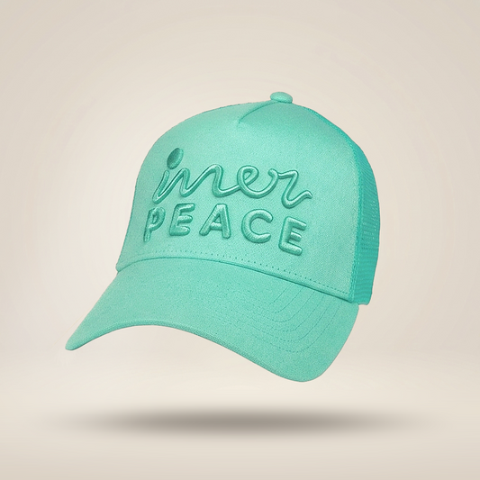A mint green trucker-style cap with 'inner peace' embroidered on the front, shown floating against a warm beige background.