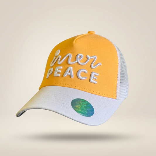 A yellow and white trucker hat with 'inner peace' embroidered on the front, set against a light beige background.