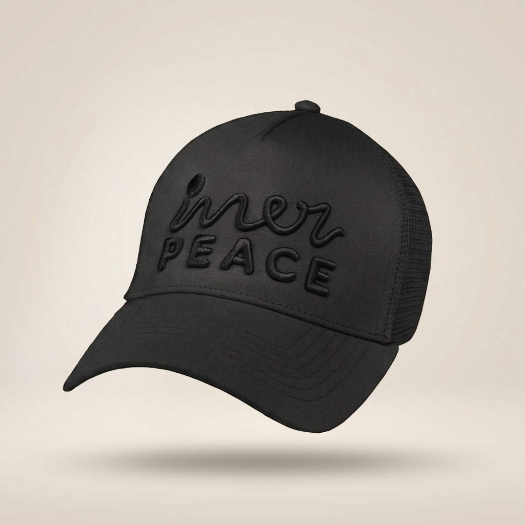 A black trucker-style cap with a curved brim, black mesh back panels, and tonal black embroidered text reading 'inner peace' on the front, shown against a light beige studio background.