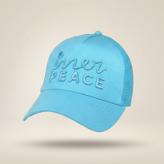 A light blue trucker-style cap with 'inner peace' embroidered on the front, shown floating against a warm beige gradient background.