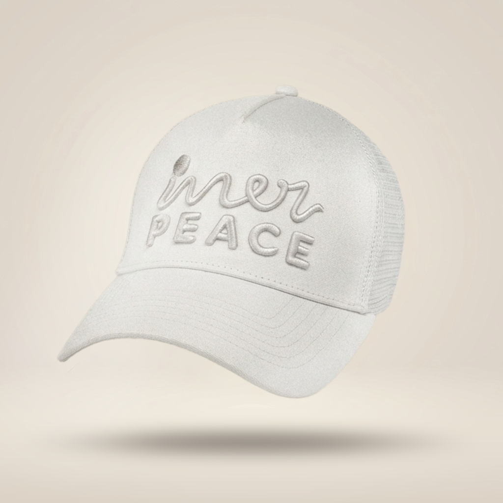 A white trucker-style cap with 'inner peace' embroidered on the front, shown floating against a warm beige gradient background.