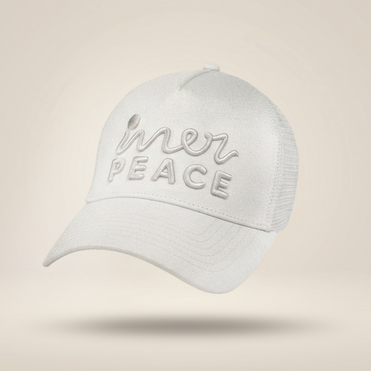 A white trucker-style cap with 'inner peace' embroidered on the front, shown floating against a warm beige gradient background.