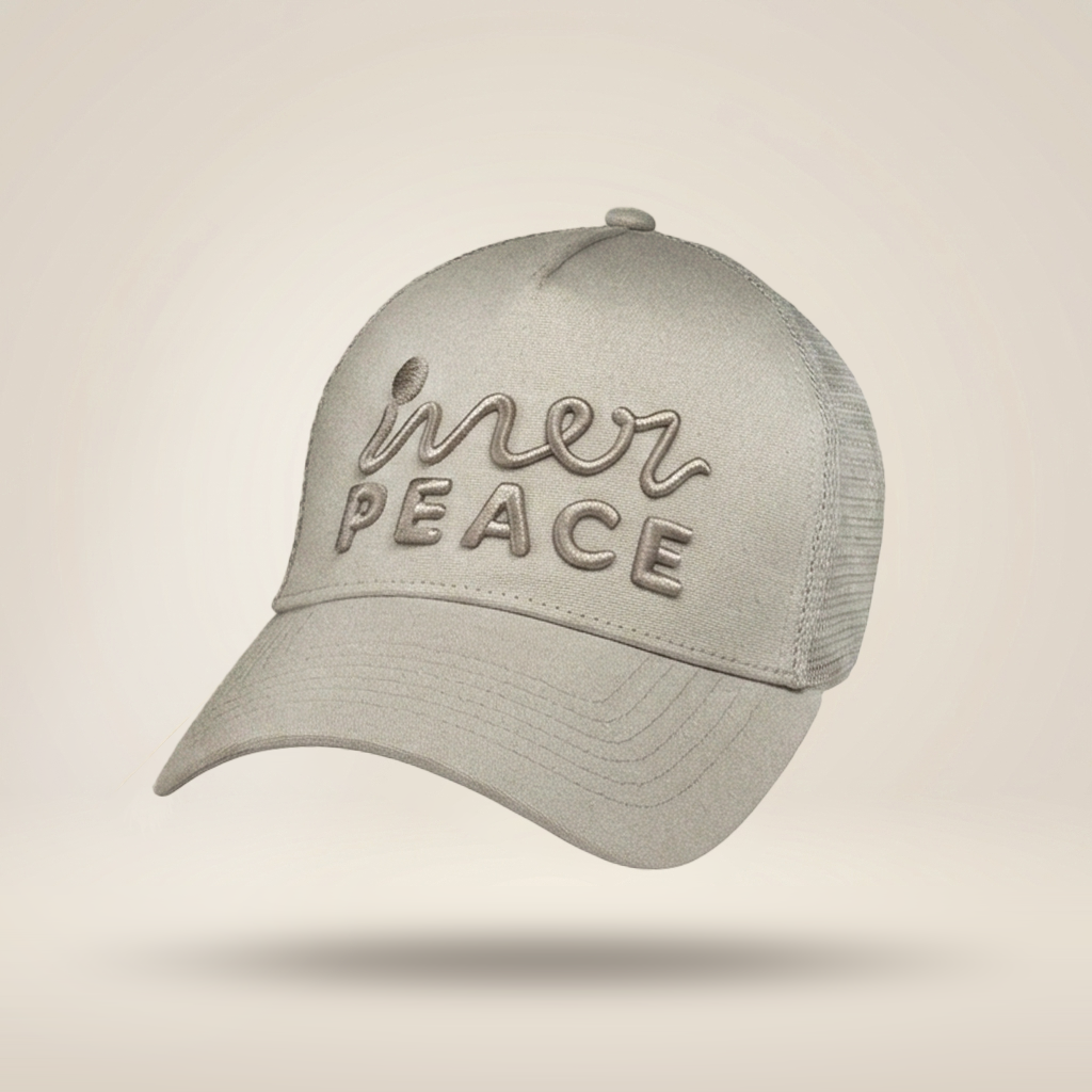 A light gray trucker-style cap with mesh back panels and embroidered text reading 'inner peace' on the front, shown floating against a soft beige gradient background.