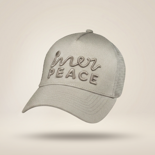 A light gray trucker-style cap with mesh back panels and embroidered text reading 'inner peace' on the front, shown floating against a soft beige gradient background.
