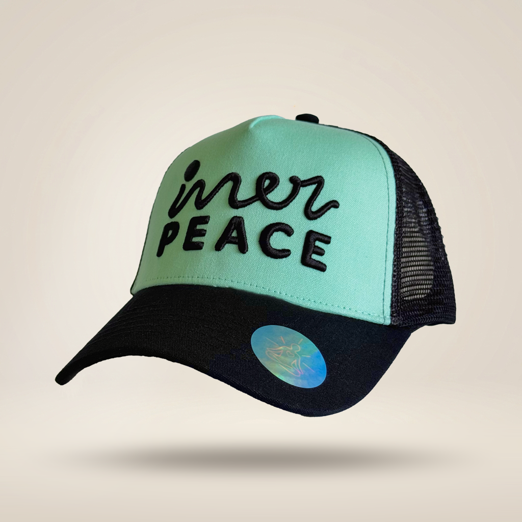 A trucker-style cap with a mint green front panel, black mesh back, and black brim. The front panel features the embroidered text 'inner PEACE' in black.