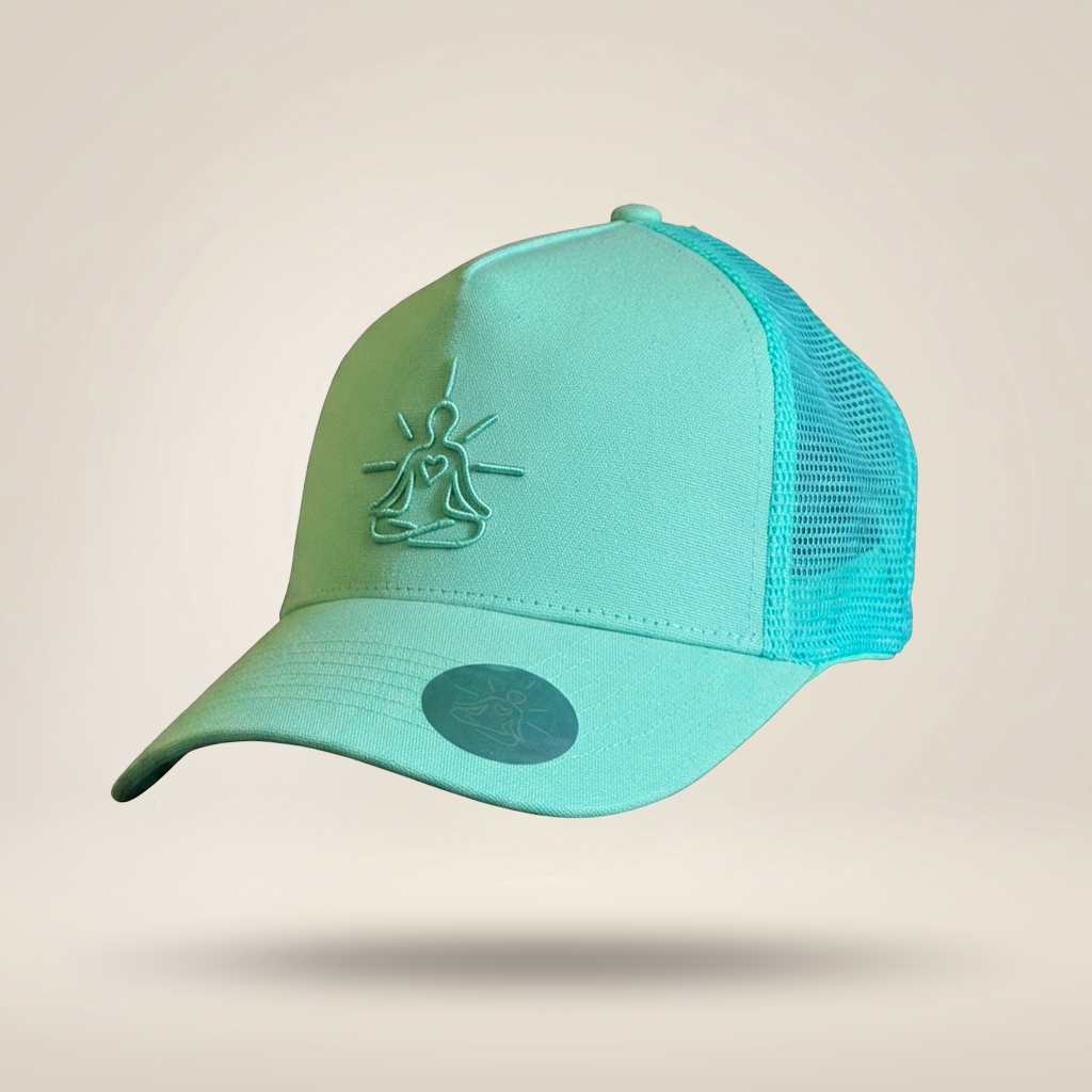 A mint green and turquoise trucker cap with a mesh back, featuring an embossed meditating figure logo on the front and a circular sticker on the brim, set against a solid beige background.
