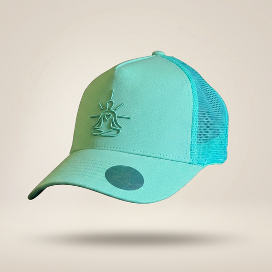 A mint green and turquoise trucker cap with a mesh back, featuring an embossed meditating figure logo on the front and a circular sticker on the brim, set against a solid beige background.